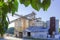 The silos and conveyors of an old concrete plant are framed by green leaves of a catalpa tree