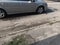 silver car drives on old muddy asphalt road