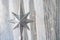 Silver Christmas star with many sparkles against a light textile curtain. Home decoration for a family holiday with copy space