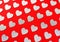 Silver confetti in the shape of heart on red background lie diagonally.