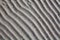 Silver gray sand on sea beach top view close up, ribbed dry sand surface pattern, wavy curved diagonal lines texture