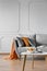 Silver, grey and orange pillows on scandinavian sofa, copy space on empty wall