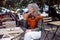 Silver haired lady with glasses uses loudspeaker mode on phone on outdoors cafe terrace