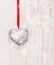 Silver heart hanging on red cord on white wooden wall , love