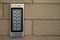 Silver intercom call panel with blue number buttons on a brick beige fence pillar of a private house