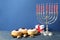 Silver menorah, dreidels with He, Pe, Nun, Gimel letters, gift box and sufganiyot on blue wooden table, space for text. Hanukkah