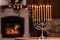 Silver menorah in room with fireplace, space for text. Hanukkah symbol