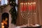 Silver menorah in room with fireplace, space for text. Hanukkah symbol