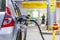 Silver metallic color car refueling on night gas station - close-up with selective focus and blurry man silhouette in