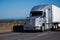 Silver modern big rig semi truck with trailer running on freeway