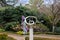 A silver and purple spherical sculpture surrounded by lush green trees and plants with blue sky and clouds