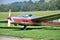 Silver and red glider stands on grass landing strip in small country airport while the weather is nice