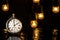 Silver retro pocket watch on a black background with a garland of glowing lightbulbs. Round antique clock on a wet