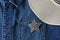 Silver sheriff star with cowboy hat on blue jean jacket