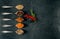 Silver spoons with various spices arranged on a slate and fruit in the middle