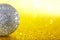 Silver toy - disco ball or Christmas decoration on a yellow background. Bokeh imitating sunbeams or rain. Macro. Abstraction.