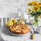 Simple apple pie, bouquet of yellow flowers, teapot on a light table on a light background