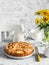 Simple apple pie, bouquet of yellow flowers, teapot on a light table on a light background