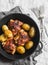 Simple baked chicken with new potatoes in a cast iron pan on grey background, top view.