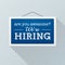 Simple blue sign with text `we`re hiring` hanging on a gray office wall. Human Resources, employment concept