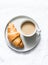 Simple breakfast or snack - coffee with milk and a classic croissant on a light background, top view