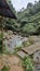 a simple bridge made of bamboo to cross a small river with rocks against the background of trees in the hills