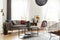 Simple brown sofa with cushions in an eclectic, white living room interior with natural light coming through big windows.