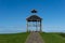 Simple gazebo pavillion with stone walkway in a green meadow under a blue sky