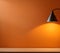Simple lamp hangs on orange wall and illuminates it, space for t