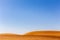 Simple minimalist desert landscape with golden sand dunes, low horizon, crystal blue sky, copy space, background