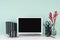 Simple minimalistic office interior with blank laptop monitor, black stationery, books, coffee cup, red bizarre twig in green mint