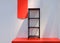 Simple modern metal black shelf unit on red platform, against white wall. Blank sales arrow banner hanging down. Beautiful light