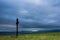 Simple oak catholic cross on green field, storm clouds over blue mountains