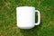 Simple plain white 11oz mug lying face up on some patchy green grass