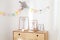 Simple posters, photo frames, wooden eco toys placed on a wooden chest of drawers stood in white interior of the children room wit