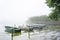 Simple rowboats moored in a row to poles on the lakeshore on a gray foggy morning, tranquil water landscape, copy space, selected