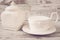 Simple rustic white crockery, empty dishes. A large cup of coffee in front angel and porcelain jar with lid. Wooden background, sh