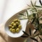 simple still life with white bowl filled with olive oil and olives and leaves from olive tree as decortation