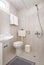 Simple style interior of small restroom with beige ceramic tile walls, white sink, classic WC toilet, grey meander ornament carpet
