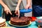 Simple sweet brown chocolate cake being cut into pieces with a knife by a woman man waiting