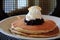 Simple white plate with stack of pancakes covered in blueberries and whipped cream