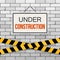 Simple white sign with text `Under Construction` hanging on a gray brick wall with warning tapes. Engineering concept