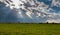 Simple wooden fence with wire on green meadow, dramatic clouds with divine lights