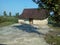 a simple, wooden-walled house on the edge of the forest. Around it there are corn plantations and teak trees. and clear blue skies