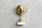 Simply flat lay design winner or champion gold trophy cup on concrete stone grey background. Victory first place of