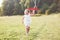 Sincere emotions. Happy little girl running on the field with red toy plane in their hands. Trees at background