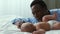 Sincere father love. Happy african american man playing with his newborn baby, lying on bed at home