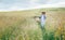 Sincerely smiling young Woman dressed jeans jacket and light summer dress walking by the high green grass meadow with basket and