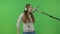 A singer with long hair sings into a studio microphone. On a green background.