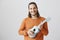 Singing song during travel in train. Portrait of friendly handsome male in orange sweater holding ukulele, playing